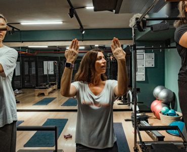 Pilates instructor guiding two women during a workout in a modern gym environment.