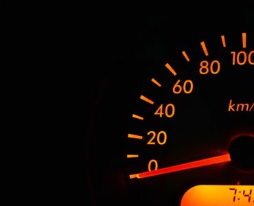 Night view of a car speedometer illuminated in orange, showing kilometers per hour.