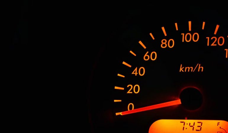 Night view of a car speedometer illuminated in orange, showing kilometers per hour.